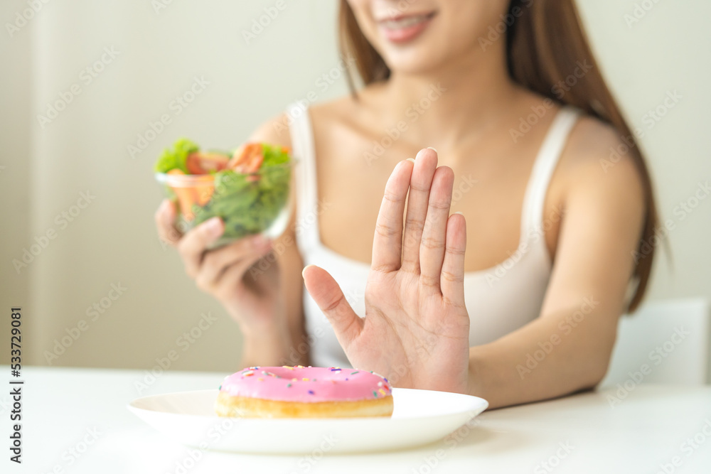 Diet, Dieting asian young woman, girl hand push out, deny sweet donut on plate, dish and choose to eat green salad vegetables in bowl on table, food good healthy, health person, female weight loss. Diet, Dieting asian young woman, girl hand push out, deny sweet donut on plate, dish and choose to eat green salad vegetables in bowl on table, food good healthy, health person, female weight loss.
