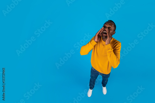 Happy black man yelling towards copy space, full length © Prostock-studio