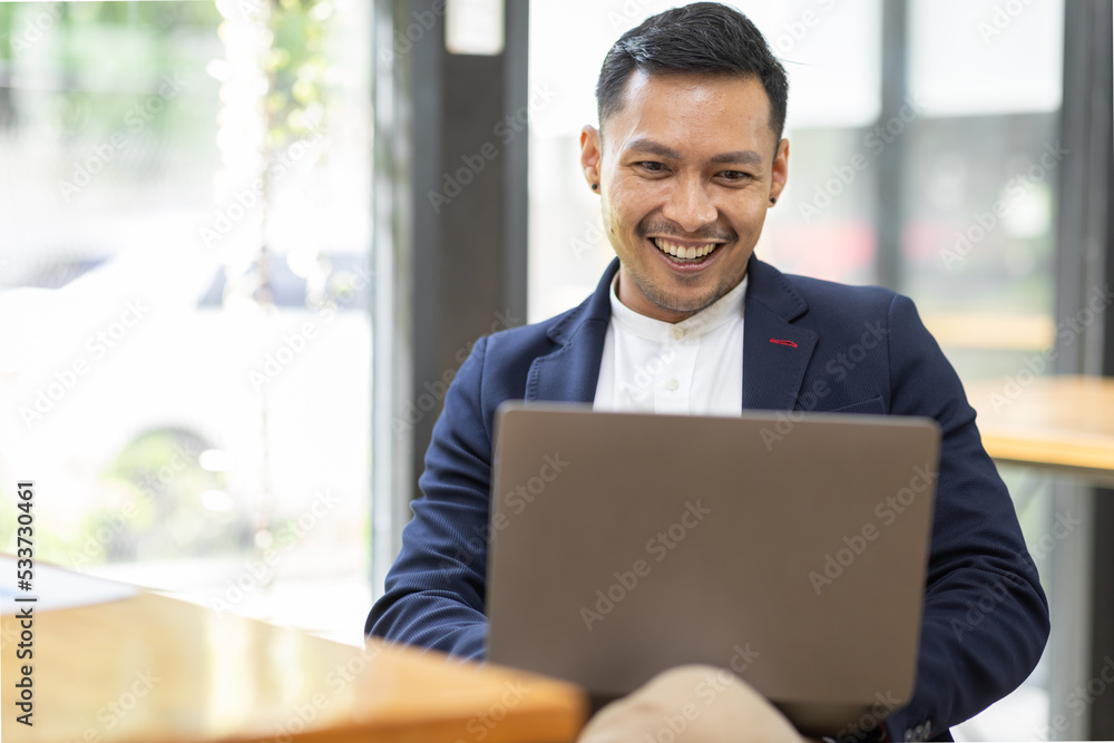 Asian Business man Using laptop computer, Successful Asian entrepreneur smiling in satisfaction as he checks information on his laptop computer while working Asian Business man Using laptop computer, Successful Asian entrepreneur smiling in satisfaction as he checks information on his laptop computer while working
