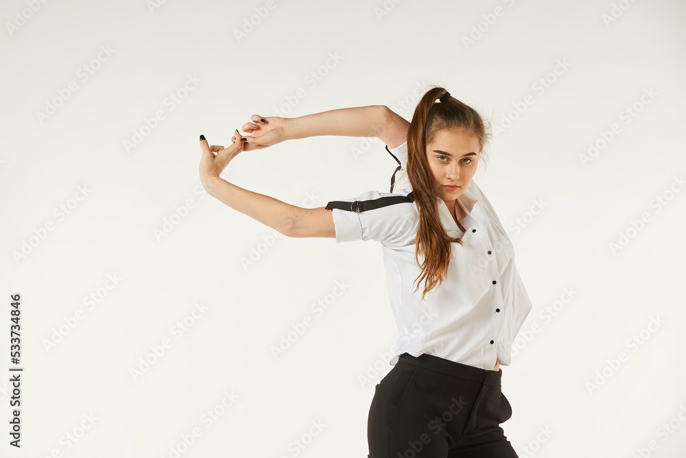 A girl in a white shirt stands on a white isolated background and does exercises.