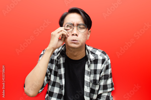 Young Asian man wearing glasses and black t-shirt and flanel with crying face expression isolated on red background. Crying face expression of Young Asian man with hand gesture.  © Teo