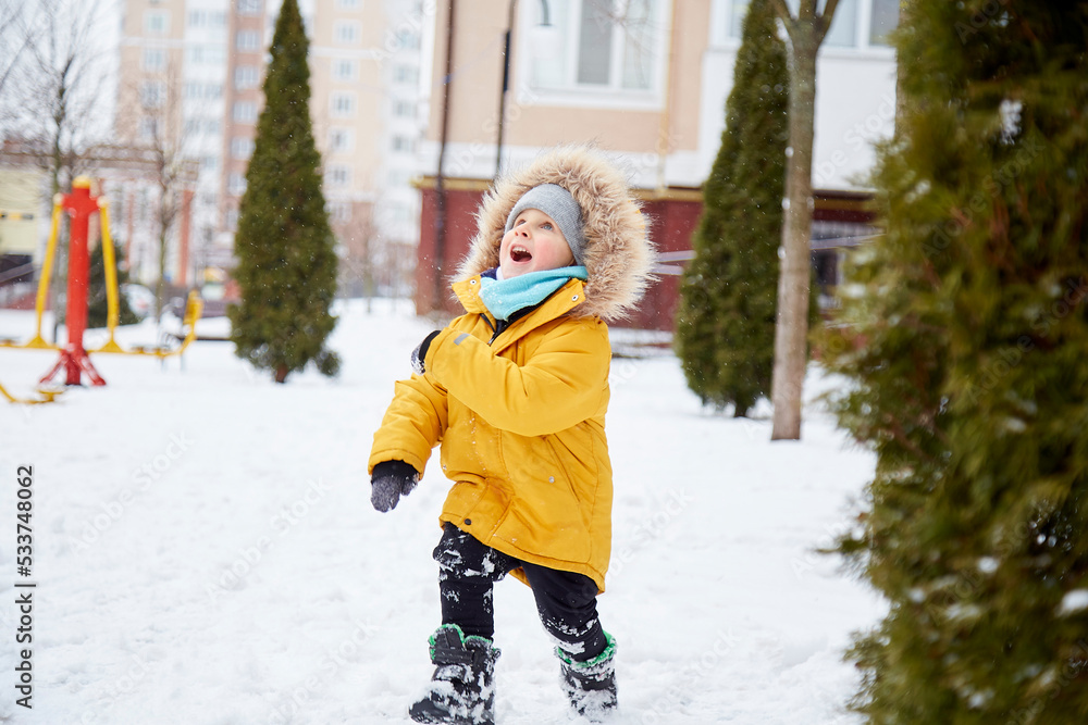 Happy child having fun in the snow in the city. Winter fun outside. Boy in bright orange winter Jacket
