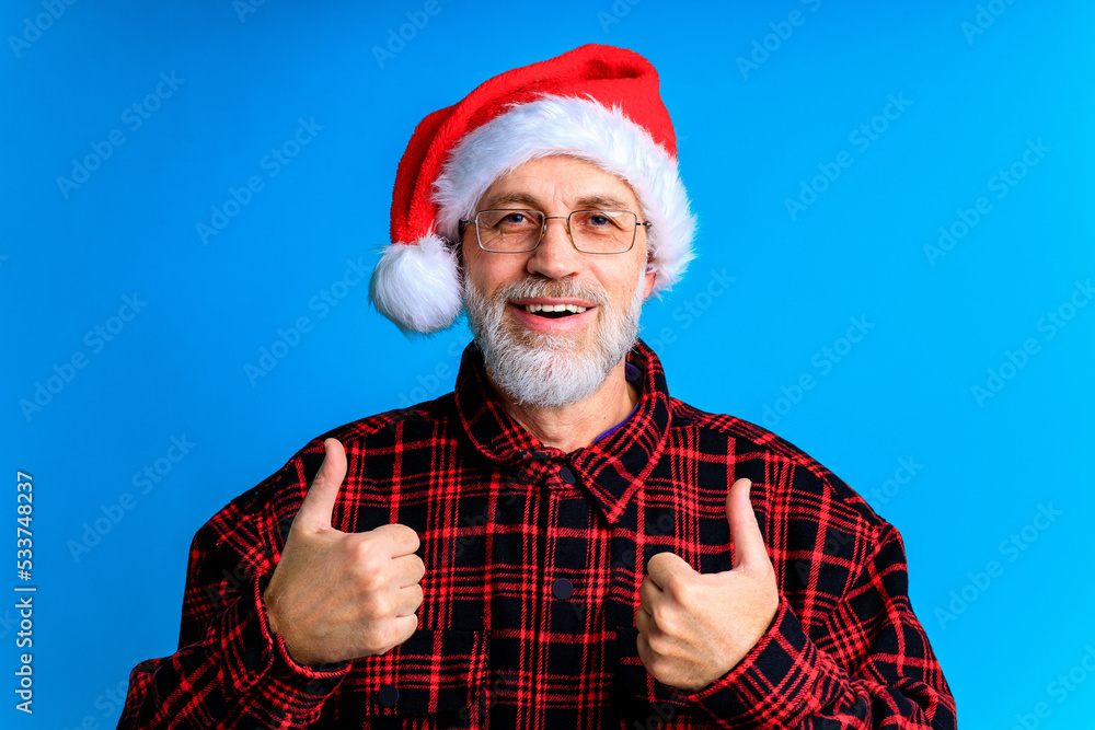 an elderly and well-groomed man in a plaid shirt and santa hat in blue studio background an elderly and well-groomed man in a plaid shirt and santa hat in blue studio background