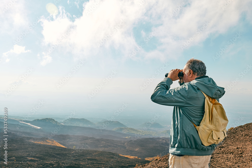 Rear view of man looking through binoculars at panoramic view of colorful summits of active volcano Etna, Tallest volcano in Continental Europe, Sicily, Italy.
