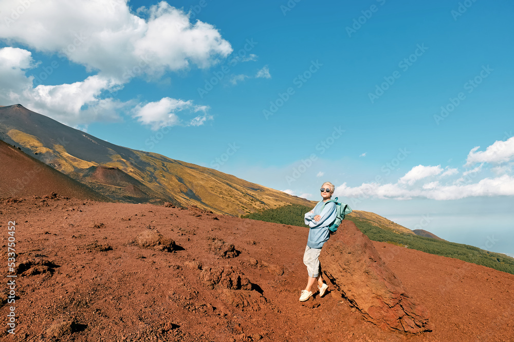 Happy tourist woman enjoying freedom, while admiring panoramic view of colorful summits of active volcano Etna, Tallest volcano in Continental Europe, Sicily, Italy.