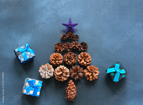 Fototapeta Naklejka Na Ścianę i Meble -  Christmas tree made of pine cones and gift boxes on dark blue background. New year Color Trends, Attention-grabbing Palettes 2023 year. DIY jewelry. Close-up
