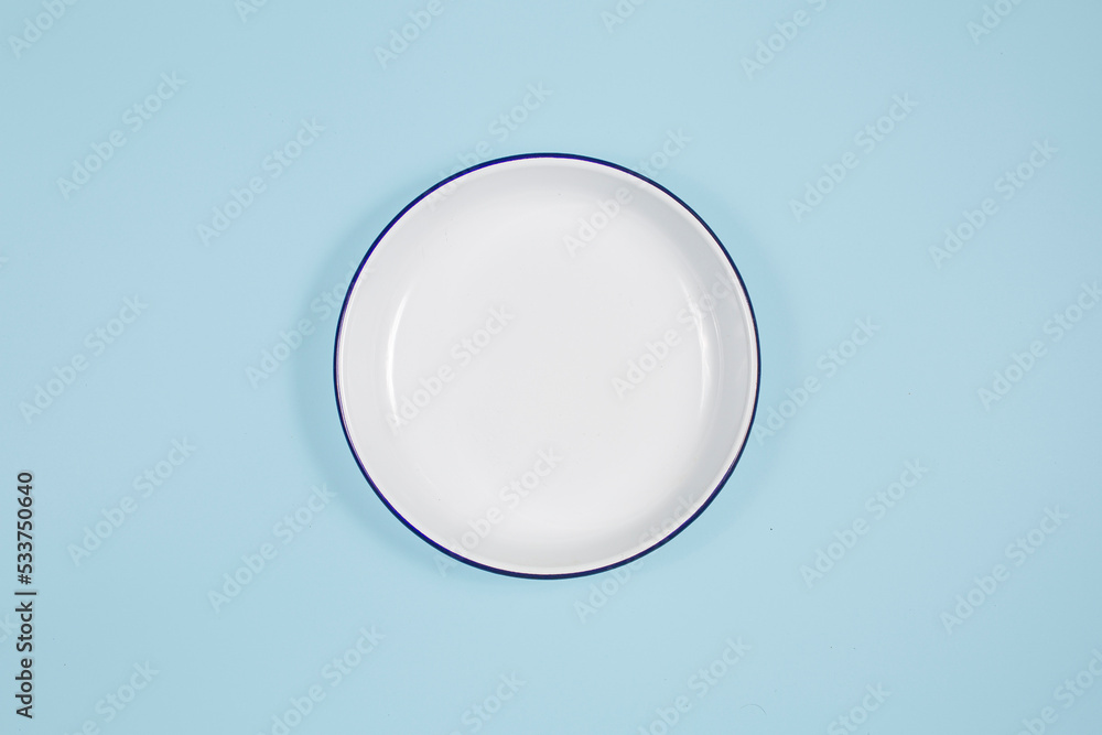 white plate in the center, top view, copy space. On a blue background - obrazy, fototapety, plakaty 