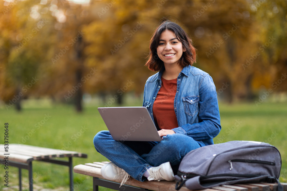 Middle Eastern Female Student With Laptop On Laps Sitting On Bench Outdoors Middle Eastern Female Student With Laptop On Laps Sitting On Bench Outdoors