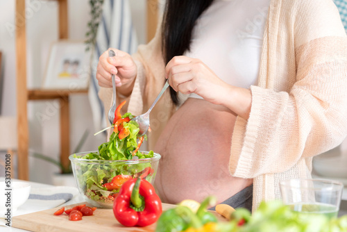 Happy asian pregnant woman cooking salad at home, doing fresh green salad, eating many different vegetables during pregnancy, healthy pregnancy concept.