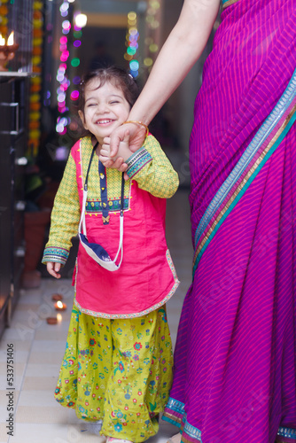 Cute little girl kid dressed up in ethnic wear feeling shy at the camera celebrating diwali Hindu festival Laxmi poojan with ambient light bokeh