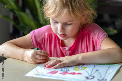Little girl drawing a picture with colored markers. Child, sitting at the desk, learning to draw.