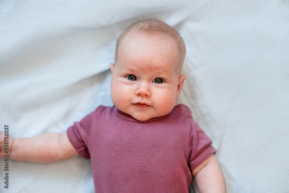 Close-up portrait of a cute Caucasian newborn baby. Charming funny baby baby looking into the camera. An authentic childhood and a candid lifestyle moment.