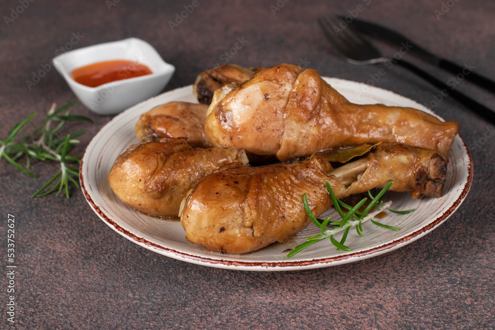 Baked chicken drumsticks in soy sauce with honey and rosemary on round plate on brown background Baked chicken drumsticks in soy sauce with honey and rosemary on round plate on brown background