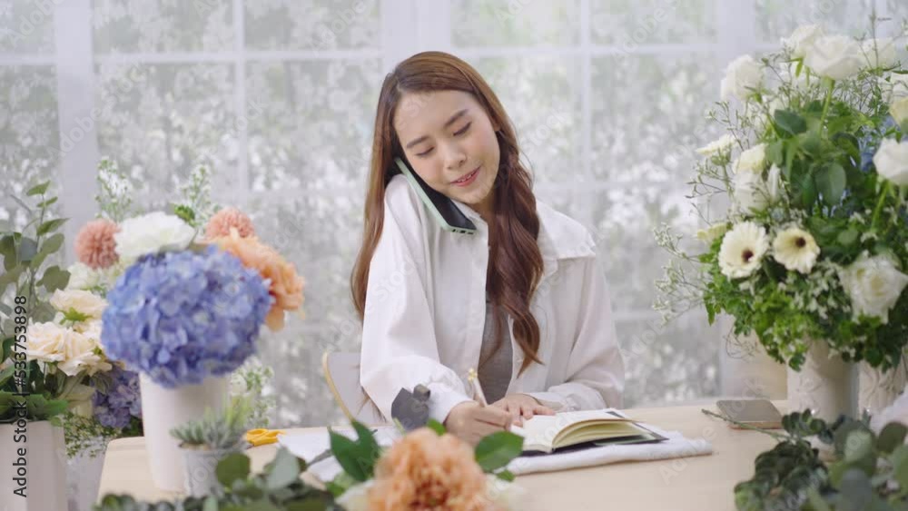 Young Asian woman stand at desk at home make beautiful floral compositions for sale. Florist talking and making beautiful bouquet of flower.