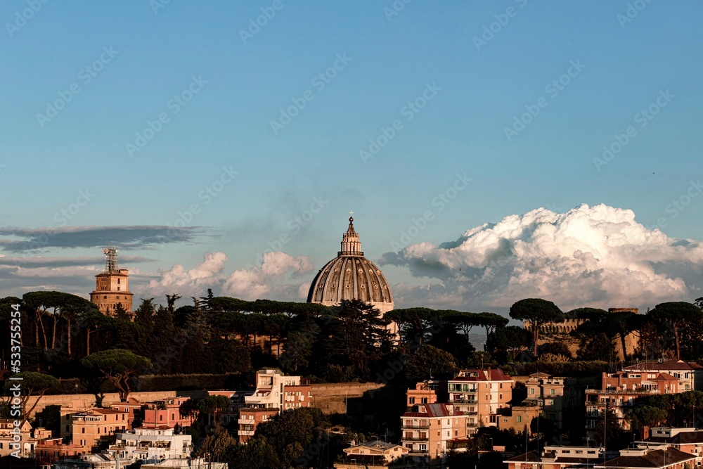 Panorama of Rome, view of the dome of St. Peter and the Vatican walls. Residential buildings in the foreground and large white clouds in the background.