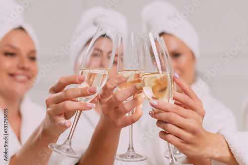 A group of women spend leisure time. Young attractive females in bathrobes drink champagne and chat merrily.
