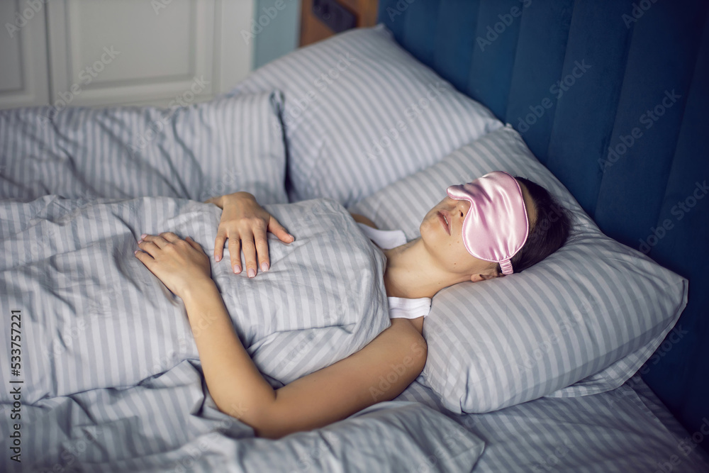 woman in a pink eye mask lies under a blanket in a bed and suffers from insomnia.