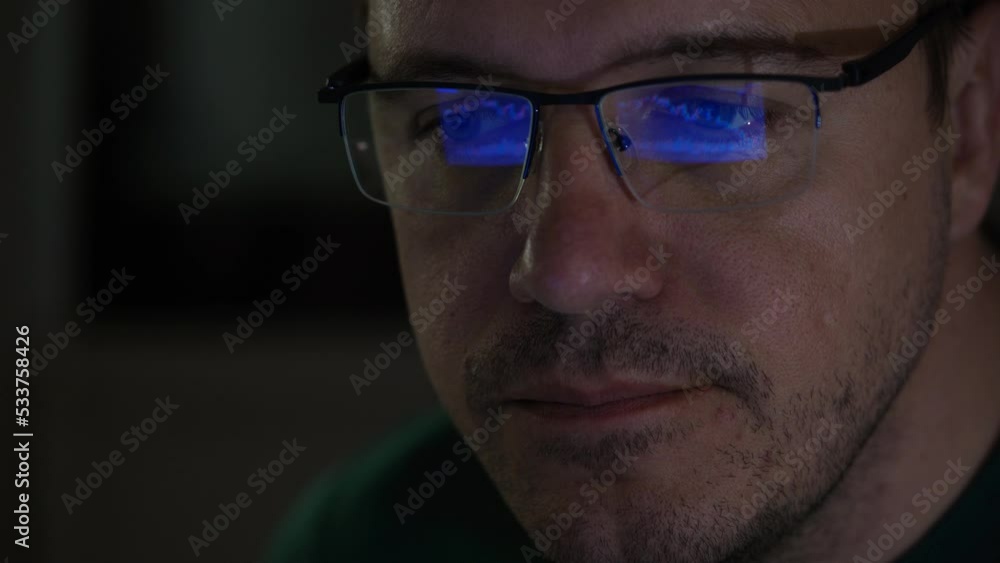 Close-up portrait of millennial concentrated trader man in glasses looks at screen with graphs in dark. Caucasian man analyst monitors exchange rate on tablet reflection in eyeglasses. Close-up portrait of millennial concentrated trader man in glasses looks at screen with graphs in dark. Caucasian man analyst monitors exchange rate on tablet reflection in eyeglasses.