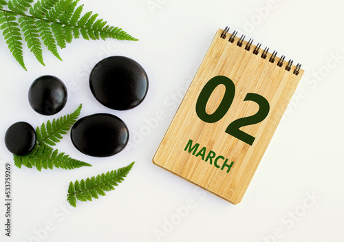 March 02. 02th day of the month, calendar date. Notepad, black stones, green leaves. Spring month, the concept of the day of year