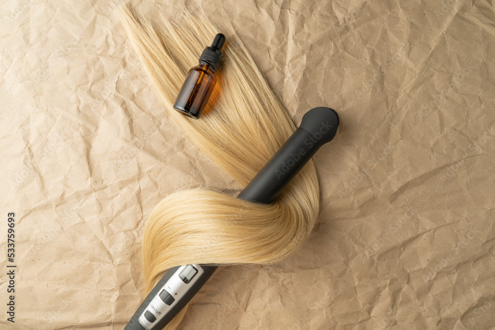 A hair treatment essential oil for smoothing hair and a hair curling styler lying on a brown craft paper background