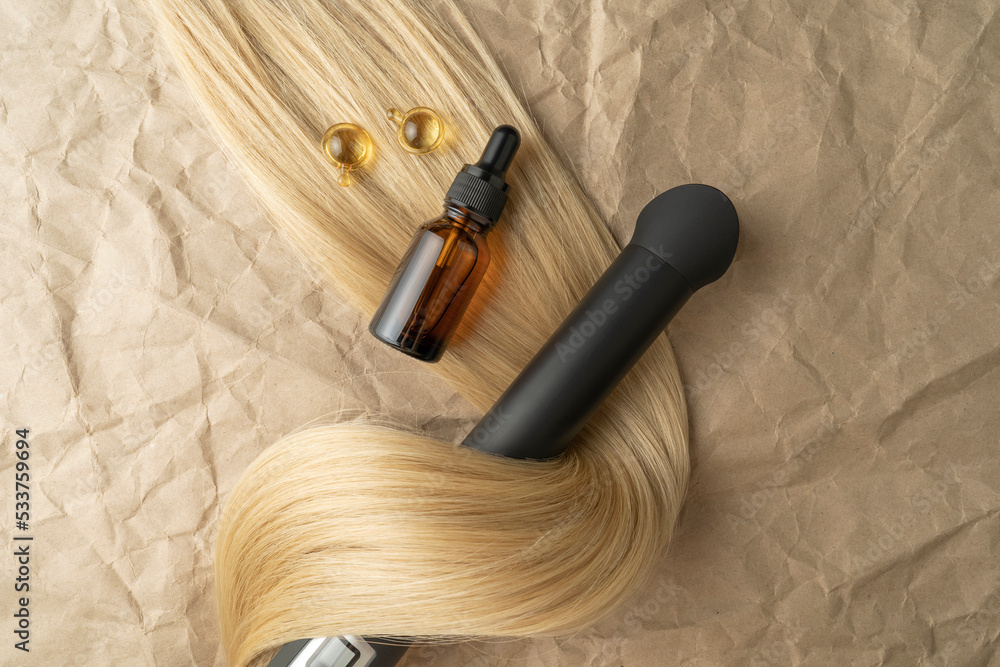 A hair treatment essential oil for smoothing hair and a hair curling styler lying on a brown craft paper background