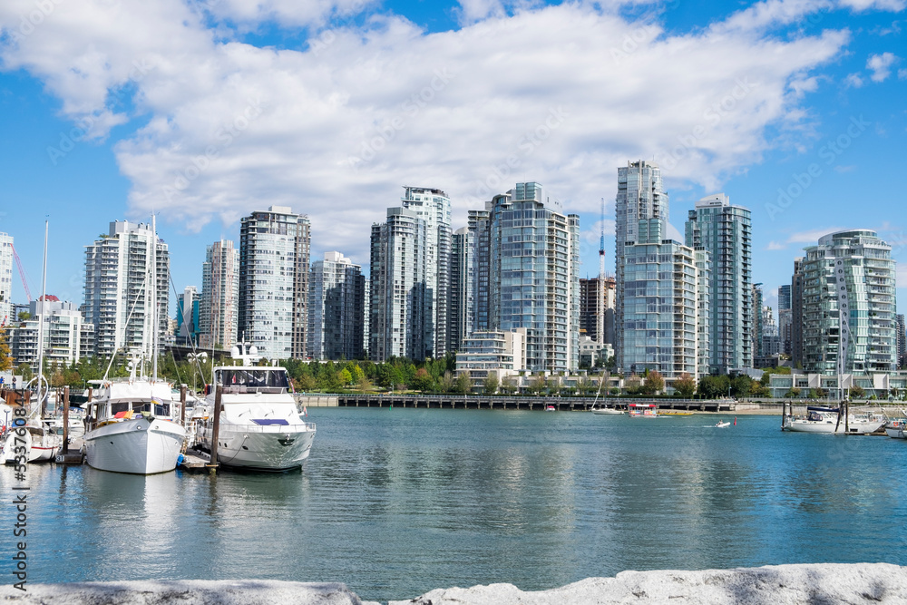 Fototapeta premium Boats sit idle in a marina on False Creek with the Vancouver's Yaletown neighborhood skyline in the background.