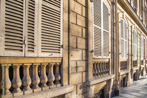 Canvas Print Closed white window shutters on top of vase-shaped balusters are warmed by the late day sunlight on an old building in Paris France