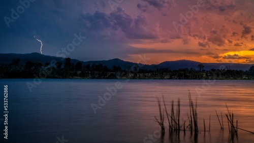 Beautiful panoramic shot of a lake under a cloudy sky with a lightning strike during the sunset