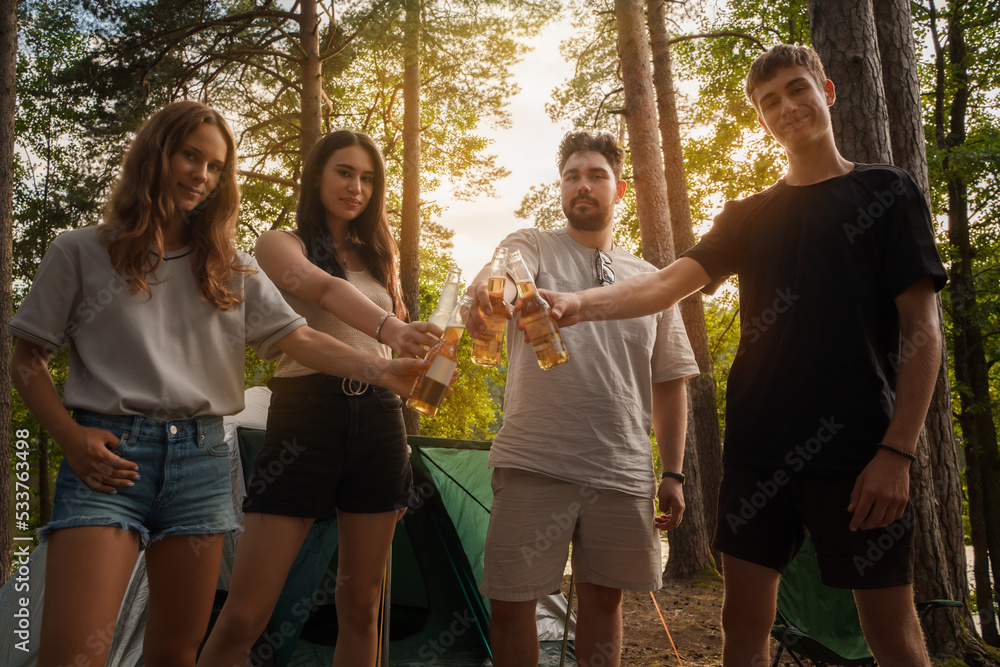 Portrait of four friends on picnic in summer wood with beer and camp.