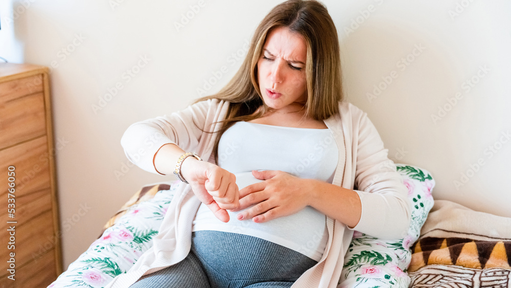 Pregnancy contractions time. Childbirth time, contractions pain. Pregnant holding baby belly, woman watching clock. Therapy, healthcare, motherhood concept.