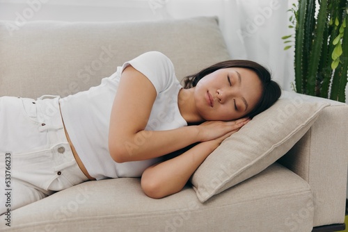 Young beautiful Asian woman sleeping on the couch at home with her eyes closed while lying on her side  resting and relaxing from stress while sleeping