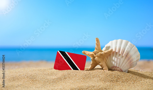 Tropical beach with seashells and Trinidad and Tobago flag. The concept of a paradise vacation on the beaches of Trinidad and Tobago.