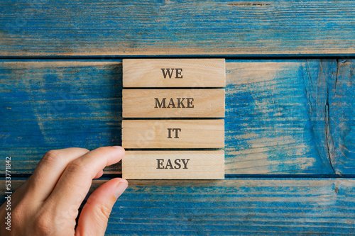 Male hand stacking four wooden pegs to make a We make it easy sign photo