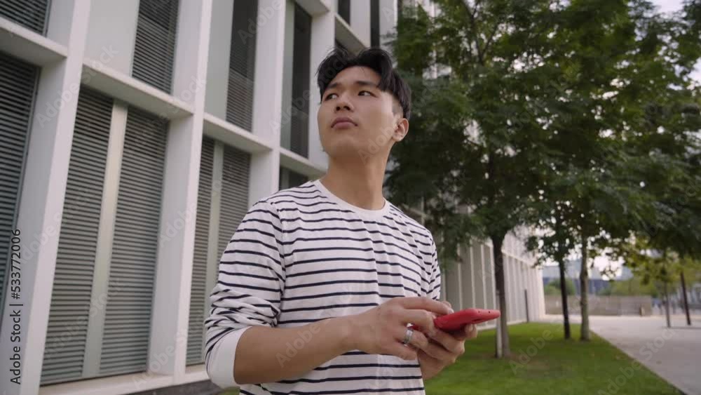 Young Asian guy navigating with mobile apps on a phone reading digital maps and searching for directions in the city. Male student and tourist while looking lost during his commute and travels in town Young Asian guy navigating with mobile apps on a phone reading digital maps and searching for directions in the city. Male student and tourist while looking lost during his commute and travels in town