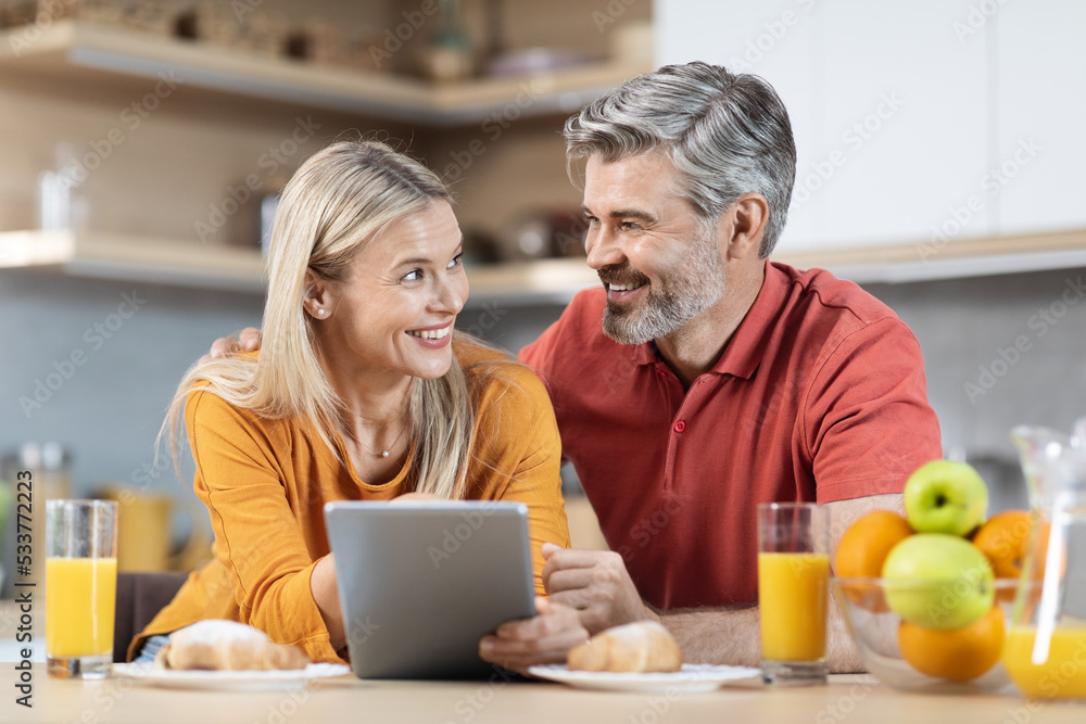 Happy couple enjoying healthy breakfast, using digital tablet Happy couple enjoying healthy breakfast, using digital tablet
