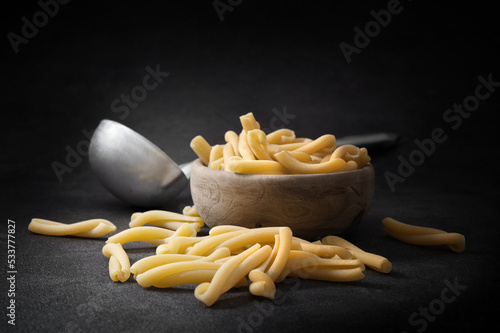 Casarecce pasta in wooden bowl with ladle on dark gray background, copy space. photo