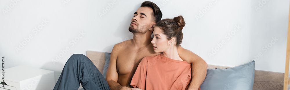 shirtless man with closed eyes embracing girlfriend in t-shirt on bed at home, banner. shirtless man with closed eyes embracing girlfriend in t-shirt on bed at home, banner.