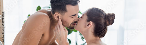 shirtless man with muscular torso kissing young girlfriend at home, banner.