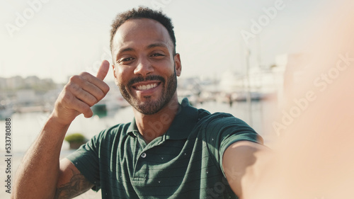 Valokuva Happy young man making video call from phone while sitting in harbor with yachts