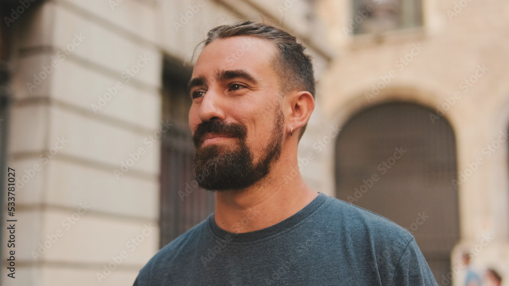 Young smiling man with beard walking and looking around at the old city background Young smiling man with beard walking and looking around at the old city background