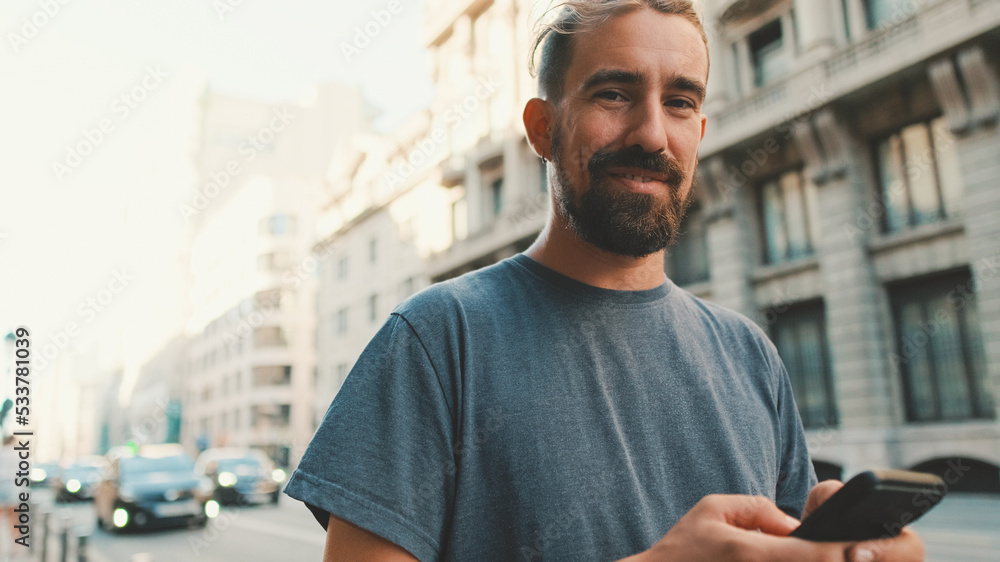 Young man with beard walks down the street using cellphone Young man with beard walks down the street using cellphone