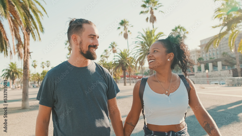 Happy interracial couple walking talking and smiling down the street holding hands Happy interracial couple walking talking and smiling down the street holding hands