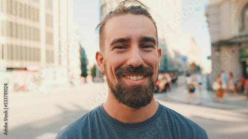 Close-up of young smiling man with beard standing in front of busy intersection