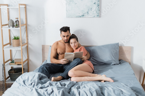 young and sexy couple reading book on grey bedding at home.