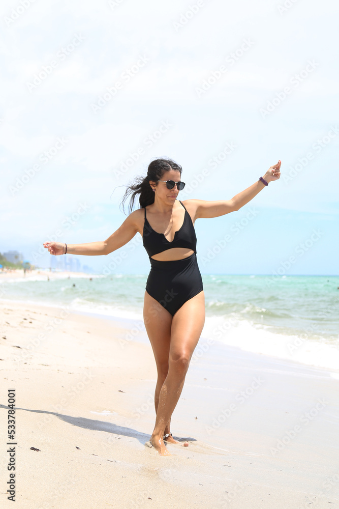Caucasian woman, beautiful and sexy, black-haired, in a black bathing suit, laughing and dancing on the shores of the sea. Vacation and fun.