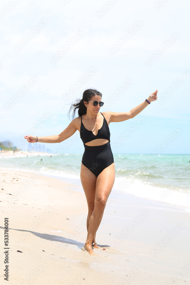Caucasian woman, beautiful and sexy, black-haired, in a black bathing suit, laughing and dancing on the shores of the sea. Vacation and fun. Caucasian woman, beautiful and sexy, black-haired, in a black bathing suit, laughing and dancing on the shores of the sea. Vacation and fun.