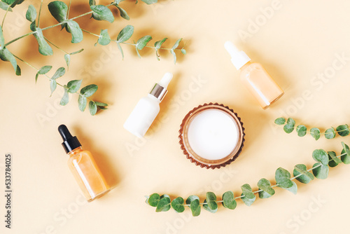 Cosmetic dropper bottles, aroma candle and eucalyptus branches on beige background. Natural cosmetics, aromatherapy and skin care concept. Top view, flat lay