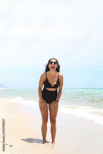 Caucasian woman, beautiful and sexy, black-haired, in a black bathing suit, laughing and dancing on the shores of the sea. Vacation and fun. © FEDEMARINIC