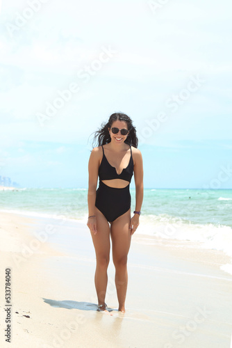 Caucasian woman, beautiful and sexy, black-haired, in a black bathing suit, laughing and dancing on the shores of the sea. Vacation and fun.