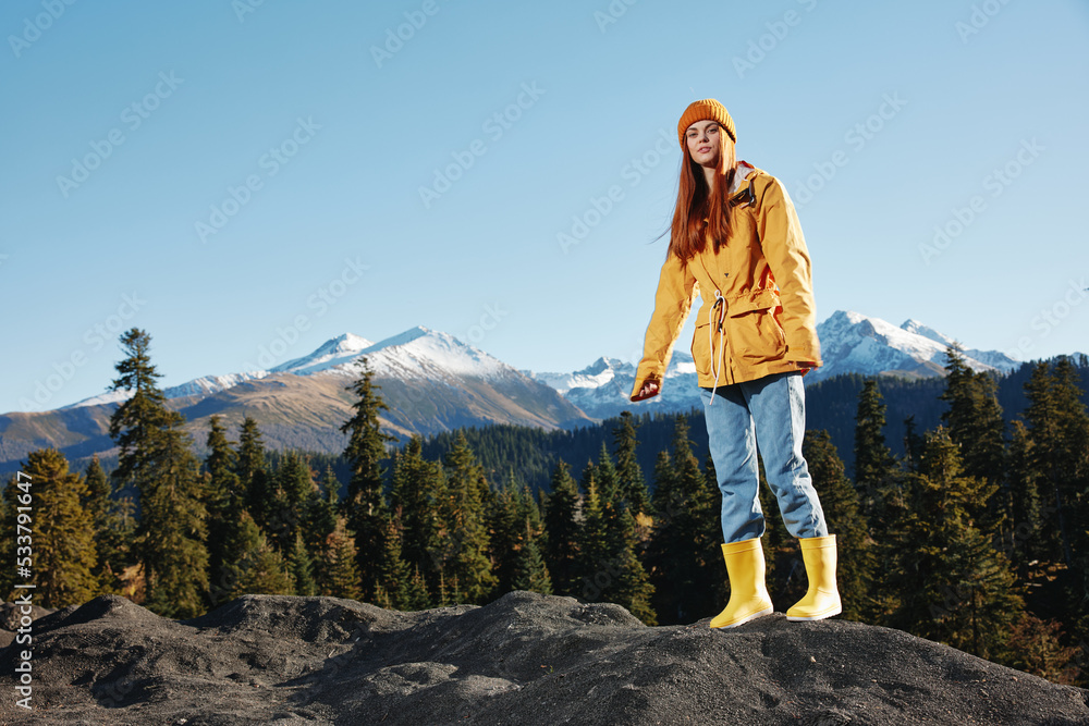 Woman in full height smile with teeth happiness hiker in yellow raincoat jumps up on the mountain trip in the fall and hiking in the mountains in the sunset freedom